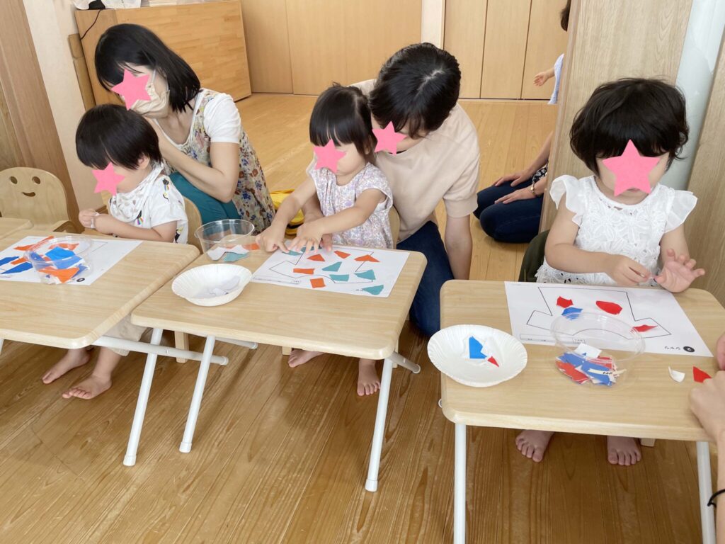 千切った折り紙を台紙に貼る親子達