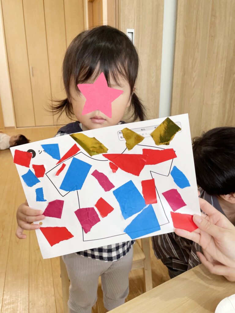 千切った折り紙で作ったシャツと写真に写る女の子